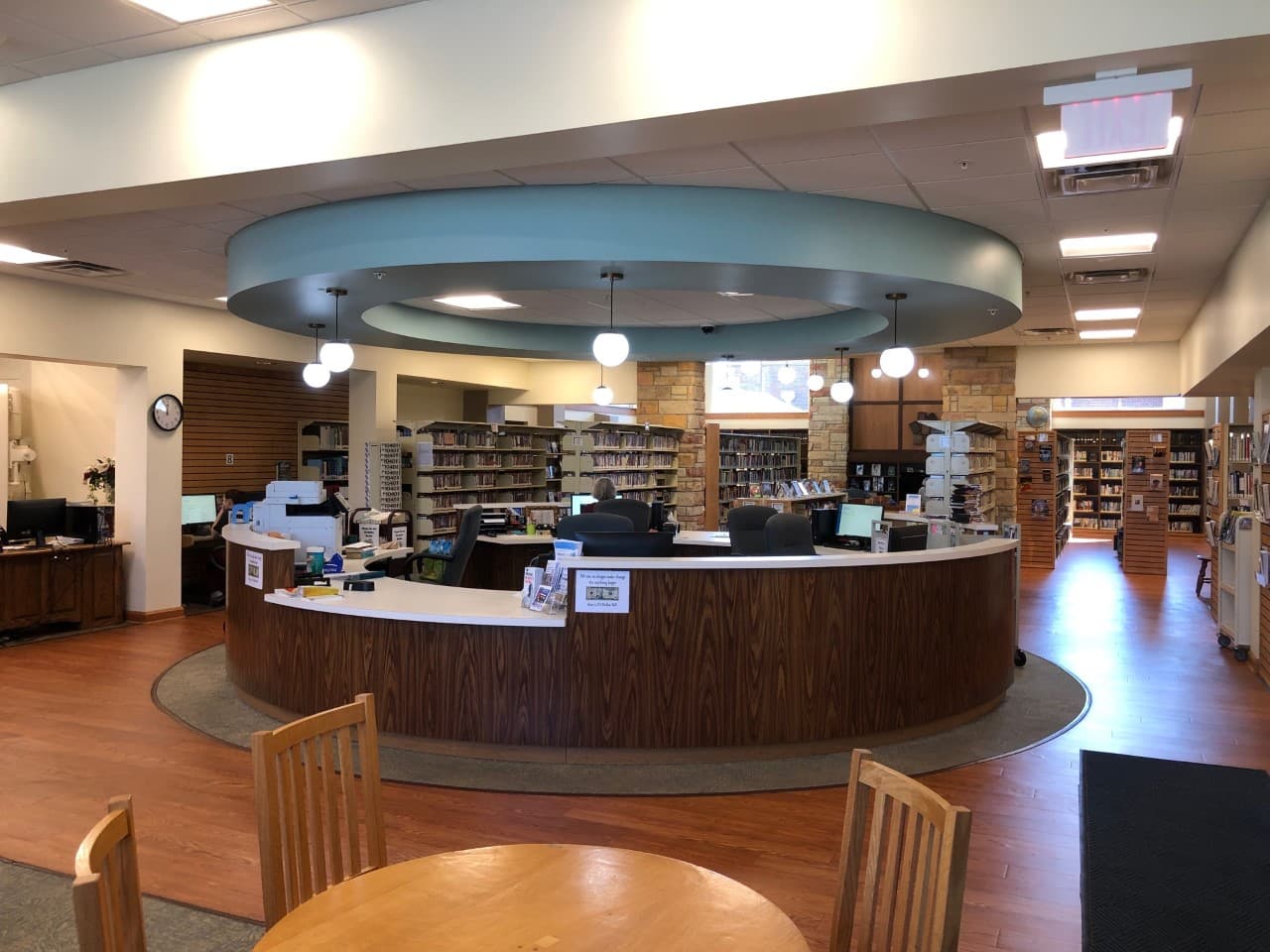 The circular circulation desk on the main floor of Owen County Public Library, with shelves and computer terminals visible behind it.