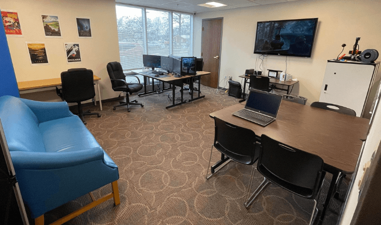 The Teen Room at Owen County Public Library: a blue lounge couch, desks with desktop computers, a wall-mounted TV for gaming consoles, posters on the wall, and additional seating around a long table.