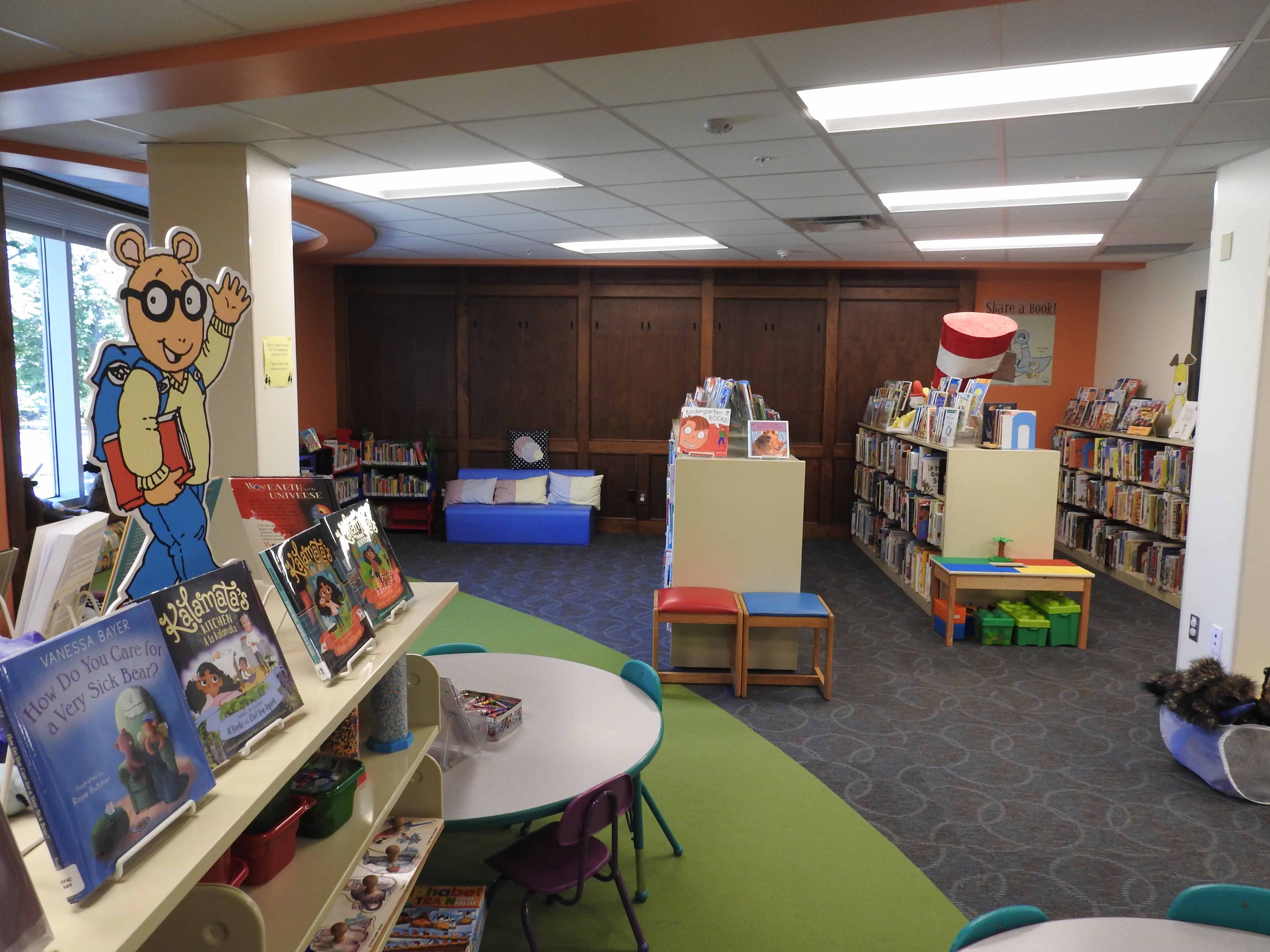 The kids' department of Owen County Public Library: a life-sized Arthur cardboard cutout, Cat-in-the-Hat decorations, low children's tables and chairs, and shelves of picture books.
